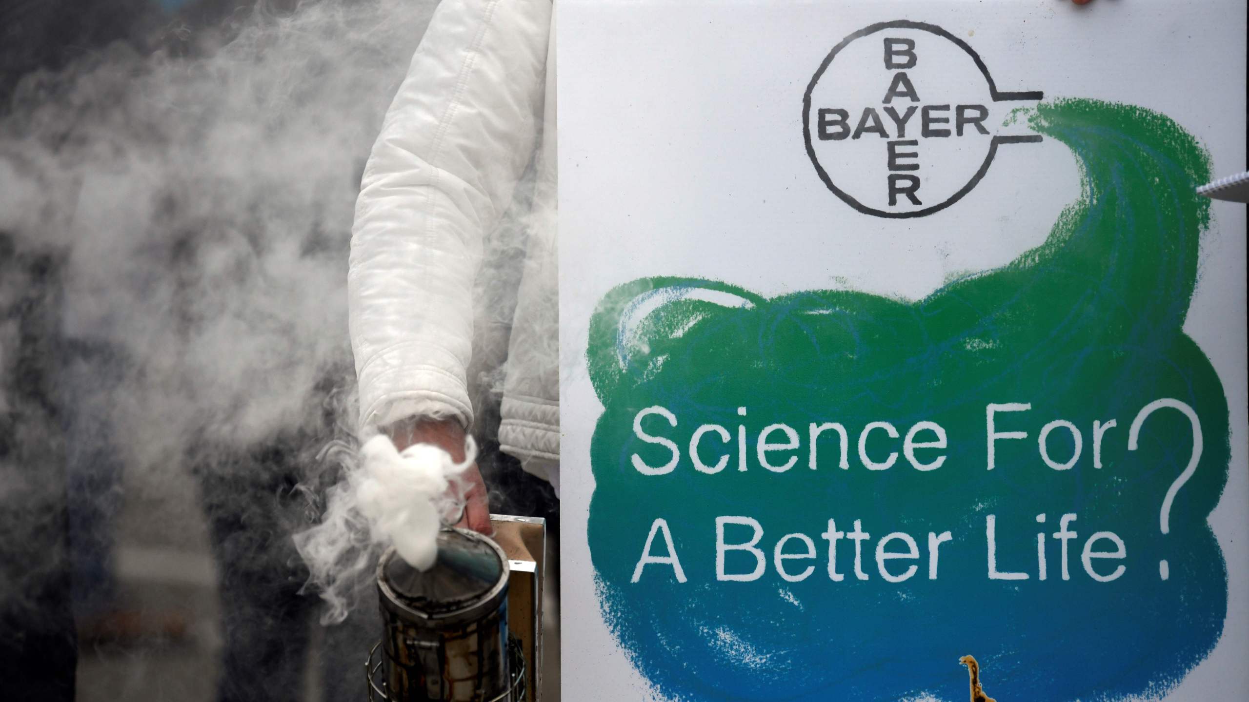 A protestor stands with a bee smoker and a placard reading "Science for a better life?" during a demonstration outside the World Conference centre where the annual general meeting of German chemicals giant Bayer takes place on April 26, 2019 in Bonn, western Germany. (Credit: INA FASSBENDER/AFP/Getty Images)