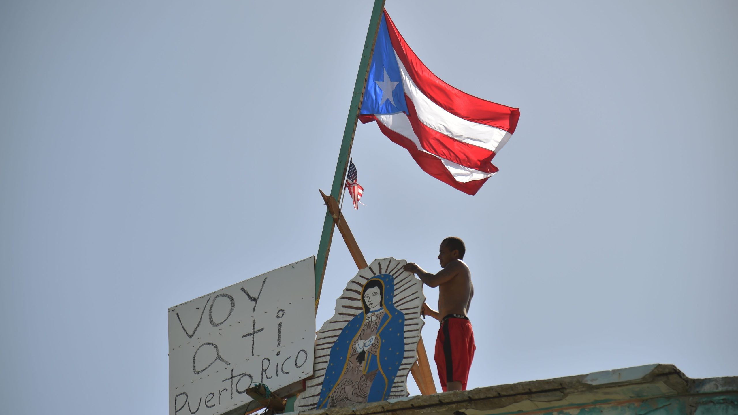 A man places on his house next to a flag of Puerto Rico, a placard that read in Spanish "Voy a ti Puerto Rico" in Yabucoa on Sept. 28, 2017.