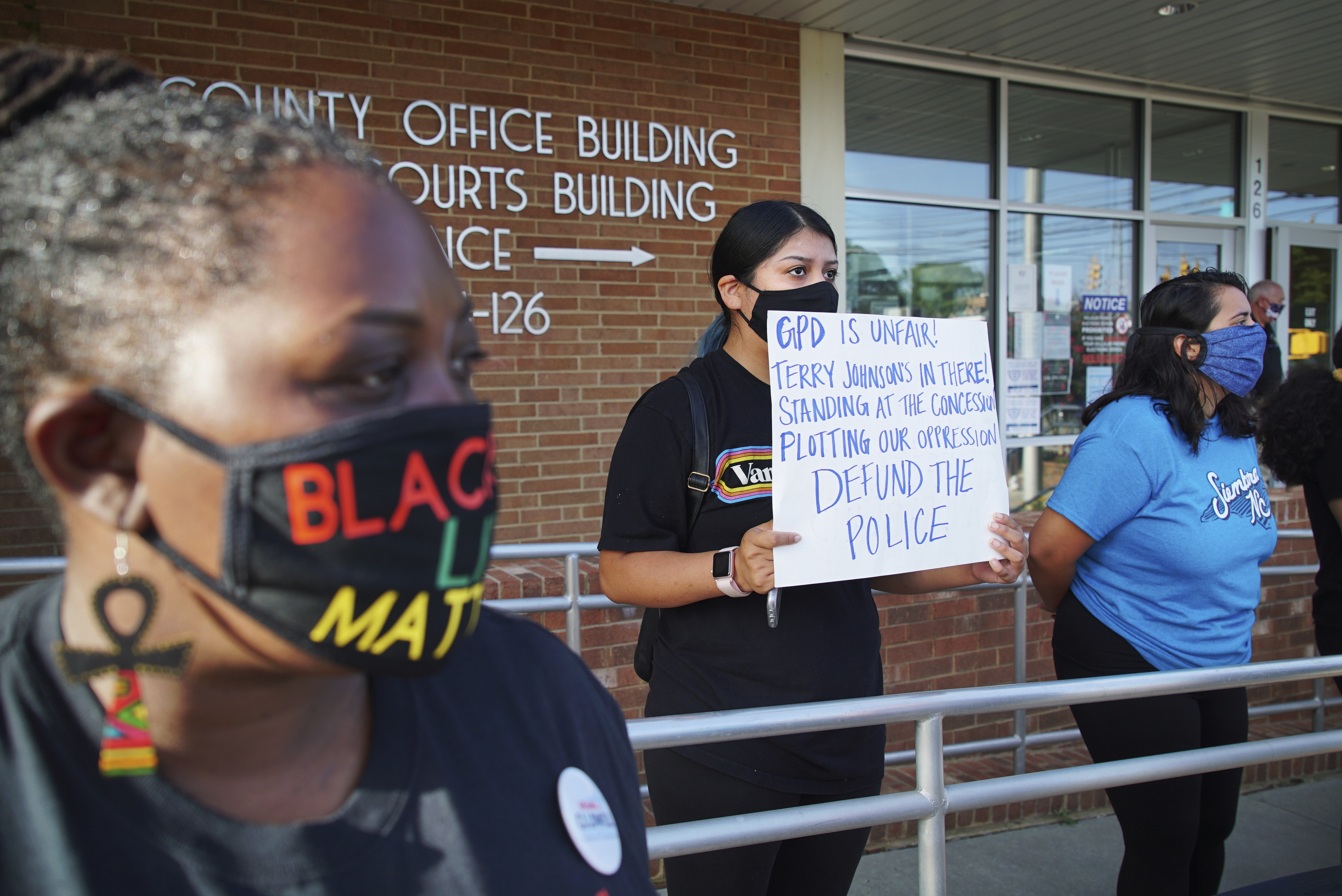 Aranza Sosa, center, holds a sign at a protest in front of the Alamance County government building in Graham, N.C., on Monday, Aug. 3, 2020. Sosa, who was born in Mexico and is now a U.S. citizen, says the county is a hostile place for people of color. (AP Photo/Allen G. Breed)