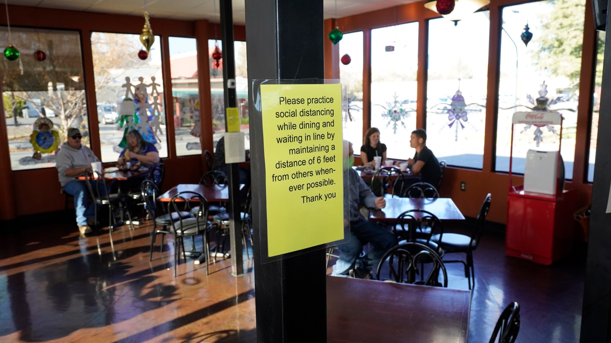 A sign advising patrons to maintain social distancing is posted in the indoor dining area of the San Francisco Deli in Redding, Calif., Thursday, Dec. 3, 2020. Brenda Luntey, who owns the deli with her husband, is openly violating the state's order to close her restaurant to indoor dining. She takes all the precautions advised, but doesn't force customers to wear a face mask. Luntey wants her customers and critics to know she is not a rule-breaker, and that it’s a matter of survival. (AP Photo/Rich Pedroncelli)