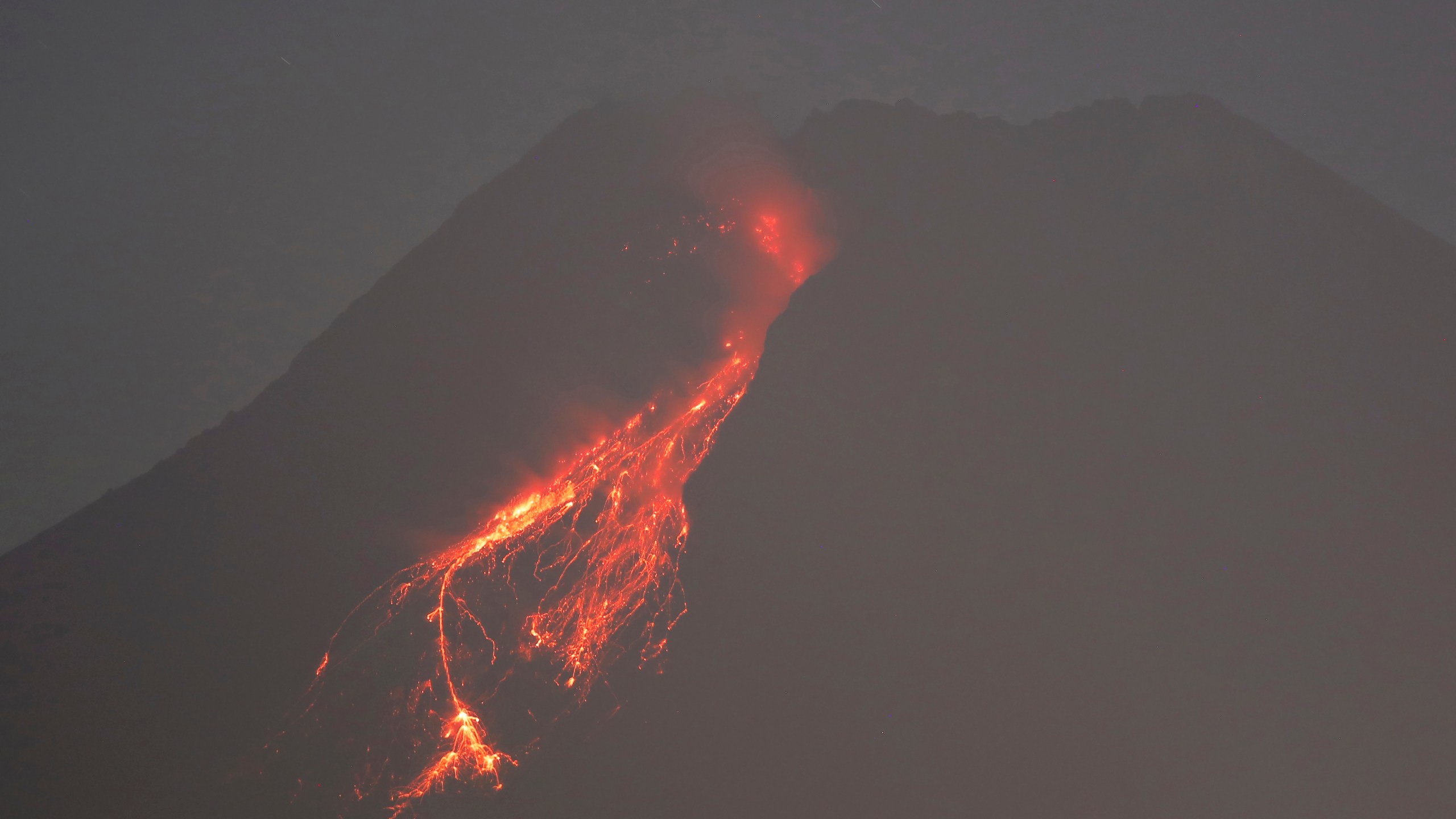 In this time-lapsed photo, hot lava runs down the side of Mount Merapi as its activity continues since local geological authority raised the alert level to the second-highest level in November, in Kaliurang, Indonesia, early Sunday, Jan. 24, 2021. Merapi is one of the most volatile among the country's more than 120 volcanoes. (AP Photo/Trisnadi)