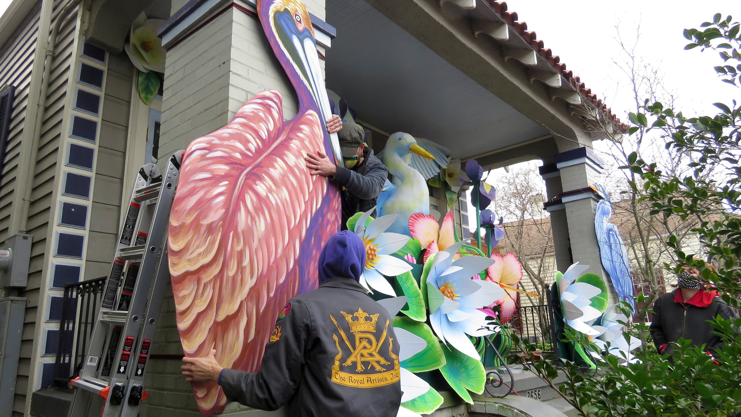 Parade float workers Travis Keene, left, and Joey Mercer position a pelican while fellow crew member Chelsea Kamm, right, looks on while decorating a house in New Orleans on Friday, Jan. 8, 2021.(AP Photo/Janet McConnaughey)