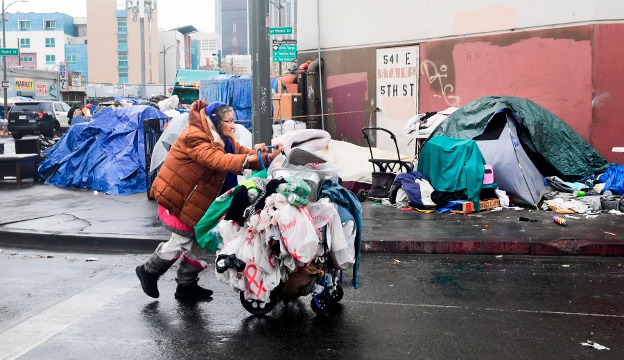 A homeless woman pushes her belongings past a row of tents on the streets of Los Angeles on Feb. 1, 2021. (Frederic J. Brown / AFP / Getty Images)