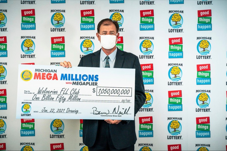 In this Feb. 26, 2021, photo provided by the Michigan Lottery, attorney Kurt Panouses poses with a check on behalf of the winners of a Mega Millions lottery jackpot in Lansing, Mich. Four people in a suburban Detroit lottery club have won a $1.05 billion Mega Millions lottery jackpot and will share $557 million after taxes. Officials made the announcement Friday, March 12, 2021, nearly two months after the Jan. 22, drawing.(Michigan Lottery via AP)