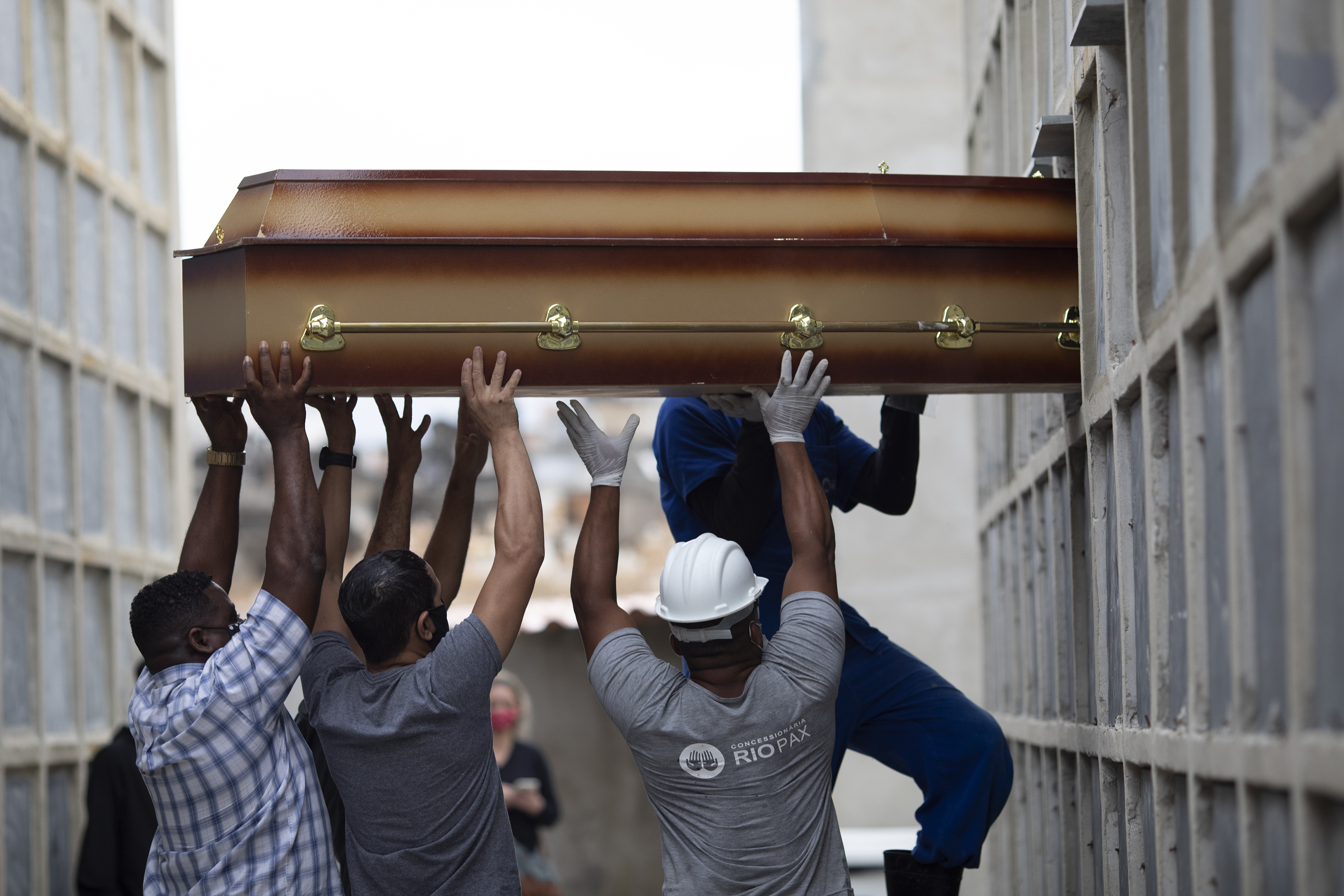 In this April 13, 2021, file photo, the remains of a woman who died from complications related to COVID-19 are placed into a niche by cemetery workers and relatives at the Inahuma cemetery in Rio de Janeiro, Brazil. (AP Photo/Silvia Izquierdo, File)