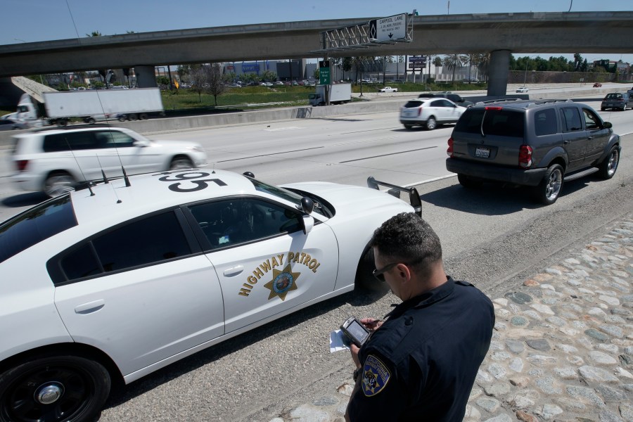 In this April 23, 2021 file photo, California Highway Patrol officer Troy Christensen runs a driver's license after stopping a motorist along Interstate 5 who was suspected of speeding in Anaheim, Calif. (AP Photo/Chris Carlson)