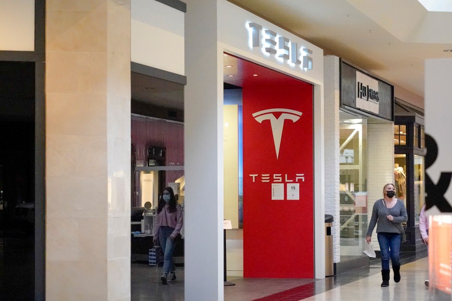 This photo made Wednesday, Feb. 24, 2021, shows people walking by the entrance to a Tesla store at a shopping mall in Pittsburgh. Tesla shares slumped about 5% in premarket trading after its CEO Elon Musk said he would sell 10% of his holdings — about $20 billion worth — in the electric car maker based on the results of a poll he conducted on Twitter over the weekend. (AP Photo/Keith Srakocic)