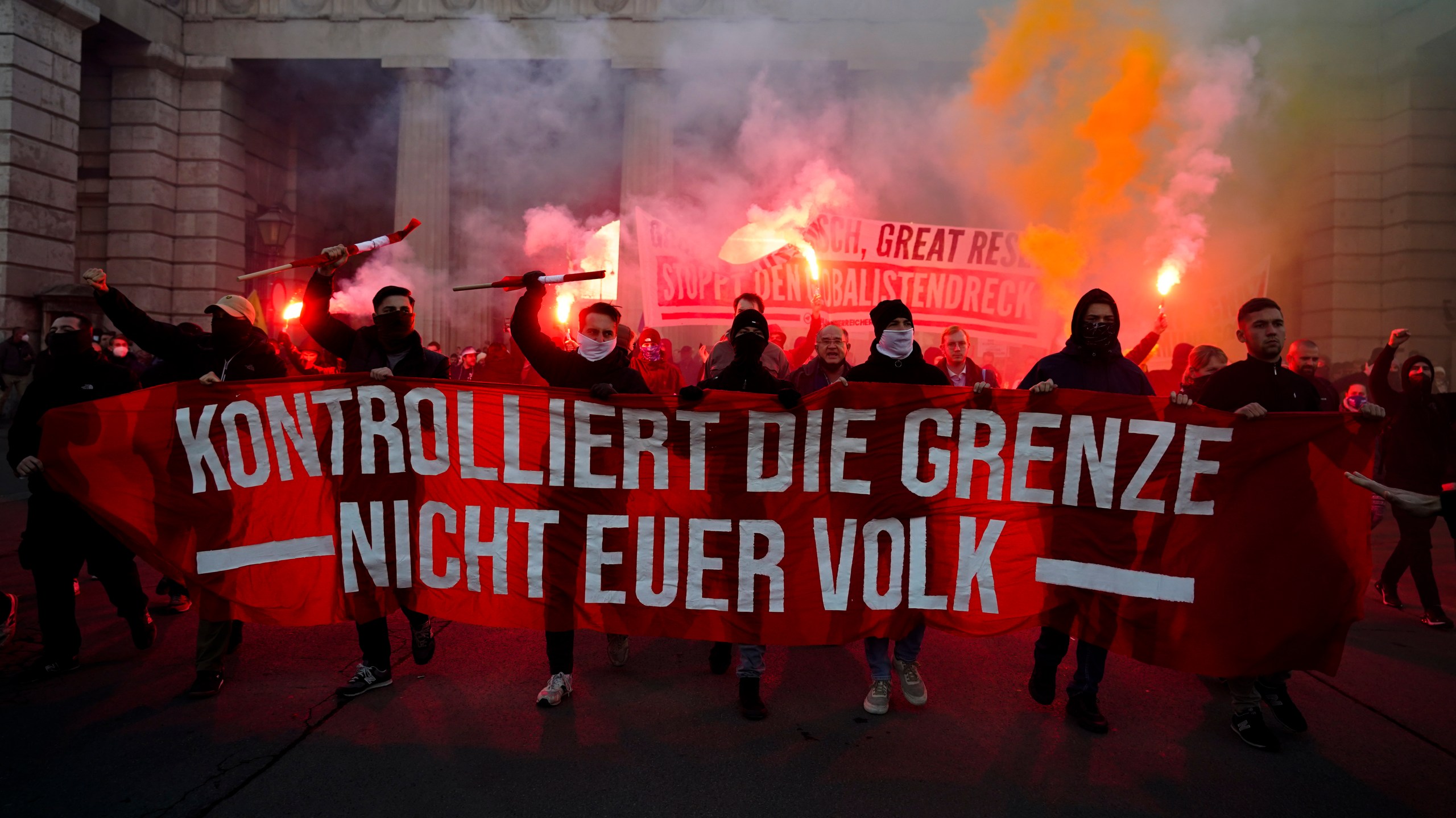 Demonstrators shout slogans and light flares during a demonstration against measures to battle the coronavirus pandemic in Vienna, Austria, Saturday, Nov. 20, 2021. Thousands of protesters are expected to gather in Vienna after the Austrian government announced a nationwide lockdown to contain the quickly rising coronavirus infections in the country. Banner reads: 'Controls the border. Not your people.' (AP Photo/Florian Schroetter)