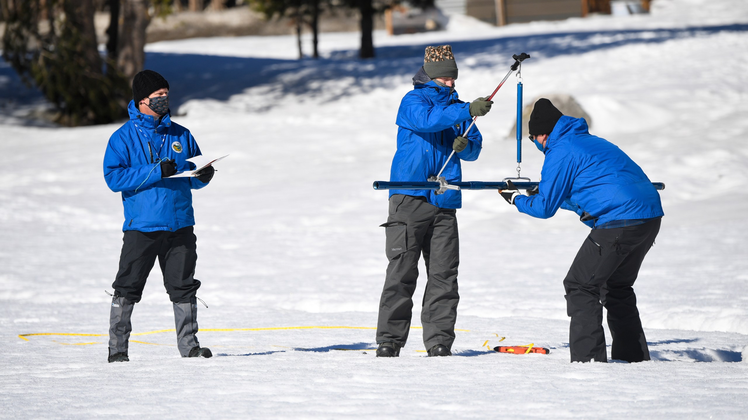 Sean de Guzman, chief of snow surveys for the California Department of Water Resources, right, places the snowpack measuring tube of a scale held by DWR's Anthony Burdock, center, as DWR's Andy Reising, left, looks on during the second snow survey of the season held at Phillips Station near Echo Summit, Calif., Tuesday, Feb. 1, 2022. The survey found the snowpack at 48.5 inches with 19 inches of snow water content. That's 109% of the historical average at this time of the year. But statewide, the water in the snowpack is 92%. (Kenneth James / California Department of Water Resources via AP)