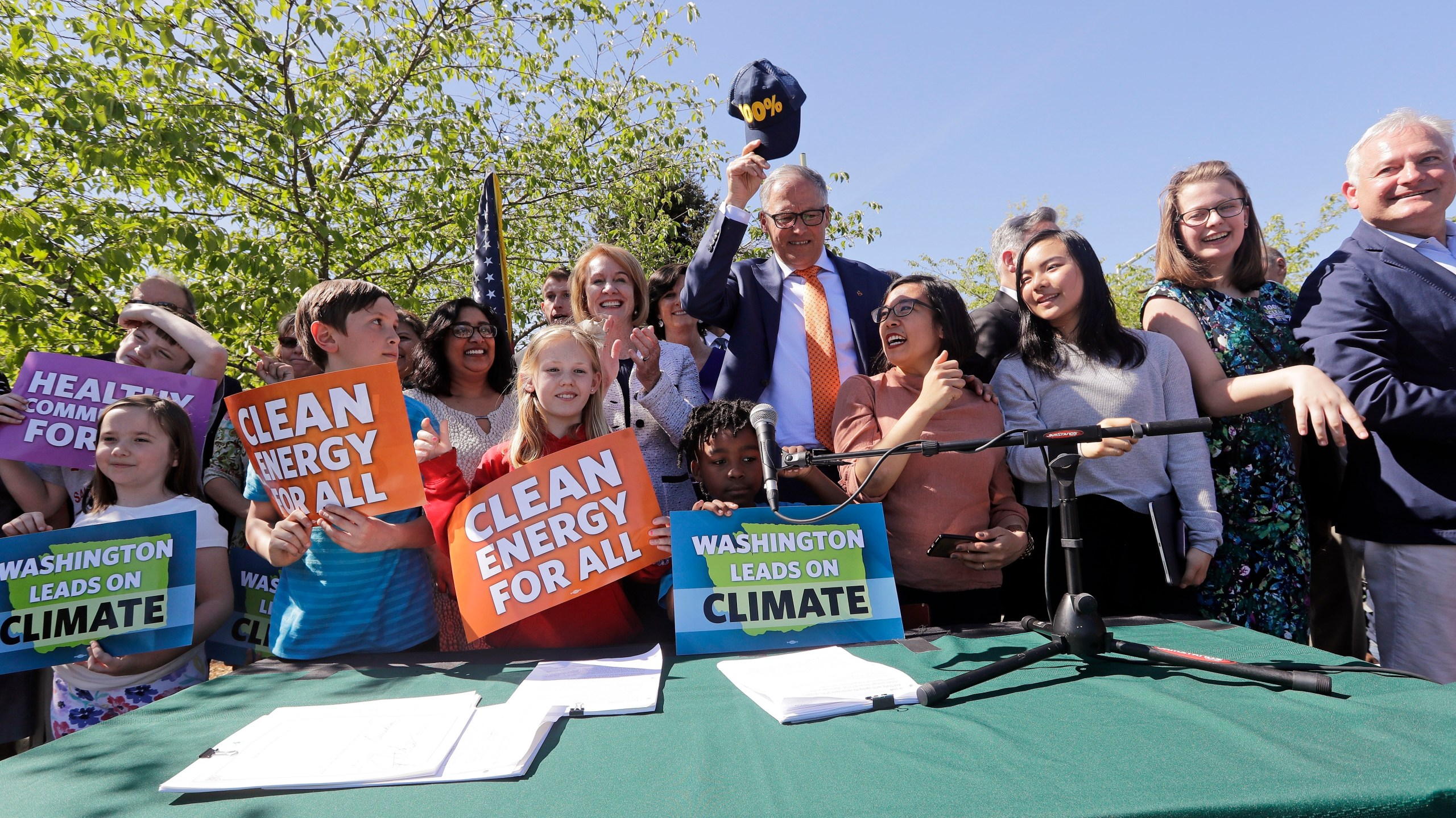FILE - Washington Gov. Jay Inslee, center, pulls off his "100%" cap, standing for a goal of 100% clean energy, after posing for a photo with supporters after signing climate protection legislation, May 7, 2019, in Seattle. (AP Photo/Elaine Thompson, File)