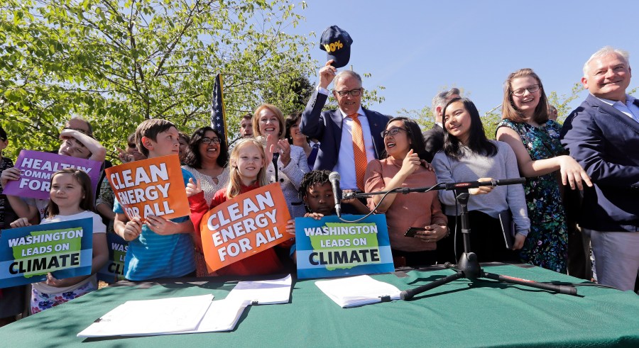FILE - Washington Gov. Jay Inslee, center, pulls off his "100%" cap, standing for a goal of 100% clean energy, after posing for a photo with supporters after signing climate protection legislation, May 7, 2019, in Seattle. (AP Photo/Elaine Thompson, File)