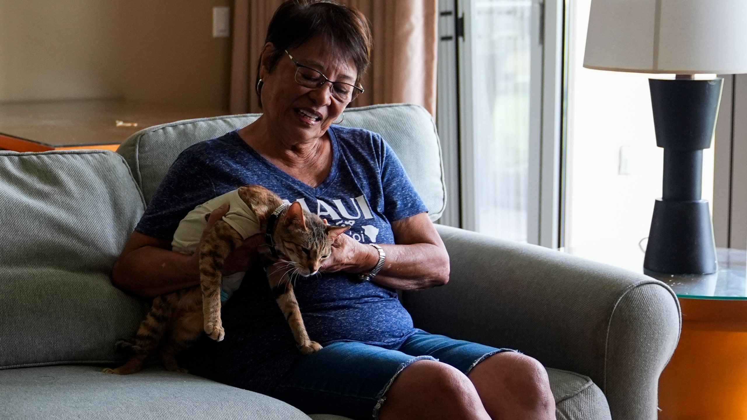 Leola Vierra holds her cat Kitty Kai in their room at the Honua Kai Resort and Spa, Wednesday, July 10, 2024, in the Kaanapali area near Lahaina, Hawaii. Vierra couldn't find their beloved cat after the 2023 wildfire. But in February, they learned Kitty Kai had found her way to Kahului, 30 miles (48 kilometers) away, across the West Maui Mountains. The reunion, while joyful, complicated their housing search. Landlords are less likely to rent to families with pets. (AP Photo/Lindsey Wasson)