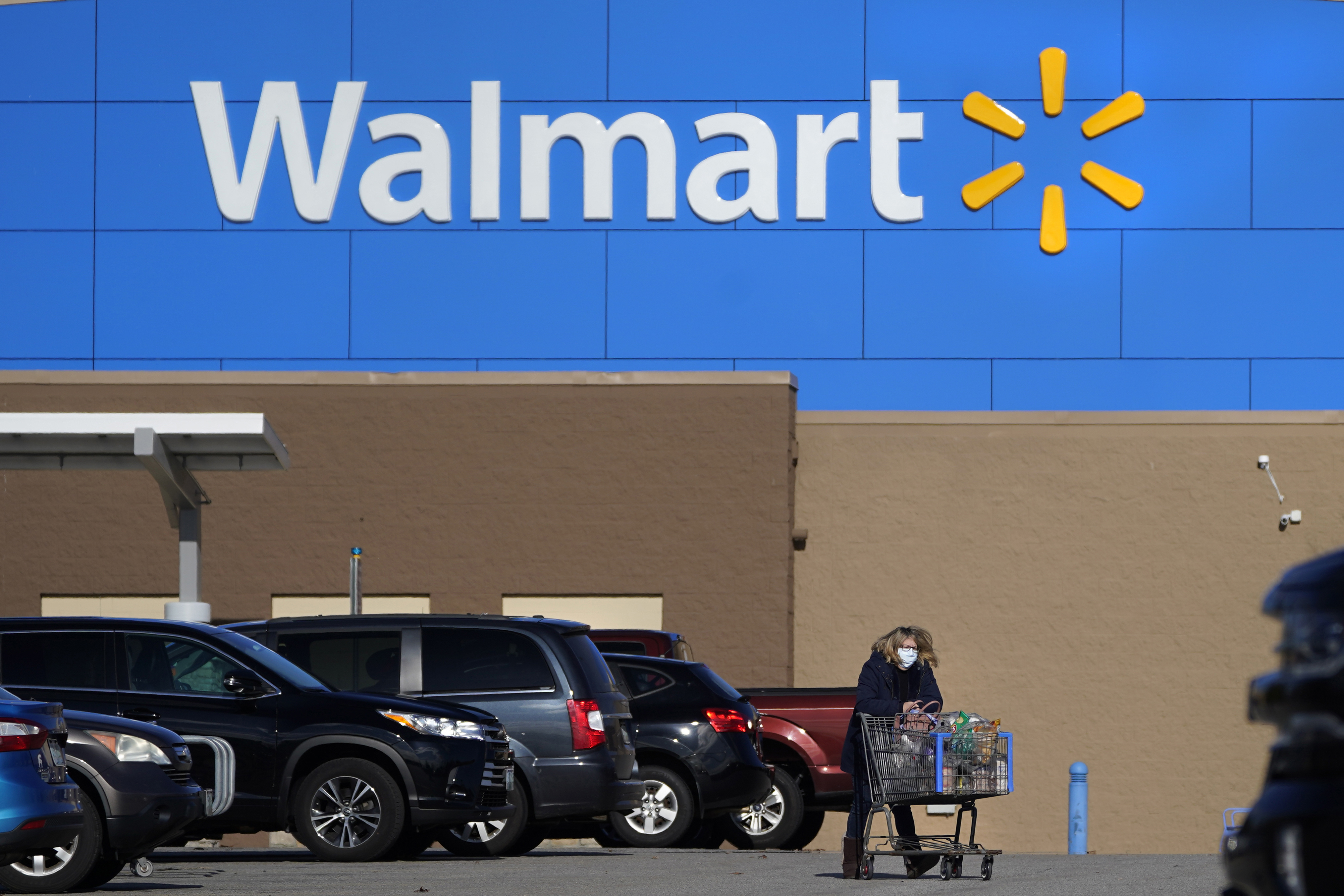FILE - A woman wheels a cart with her purchases out of a Walmart store, Nov. 18, 2020, in Derry, N.H. (AP Photo/Charles Krupa, File)