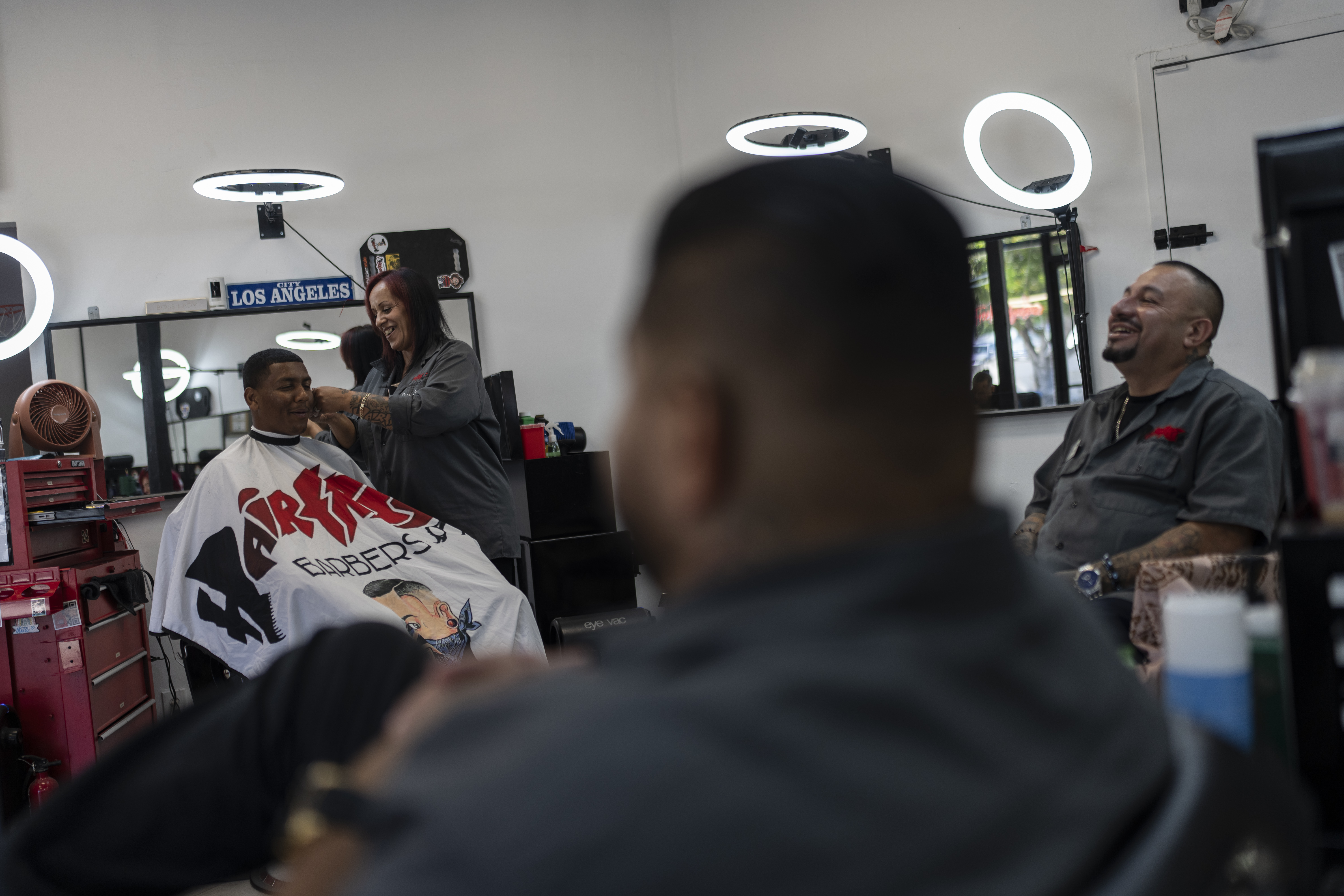 Adelita Valentine, second from left, owner of HairFreek Barbers, shares a light moment with other barbers while giving a haircut to Cameron Loualhati in Los Angeles, Wednesday, Aug. 21, 2024. (AP Photo/Jae C. Hong)