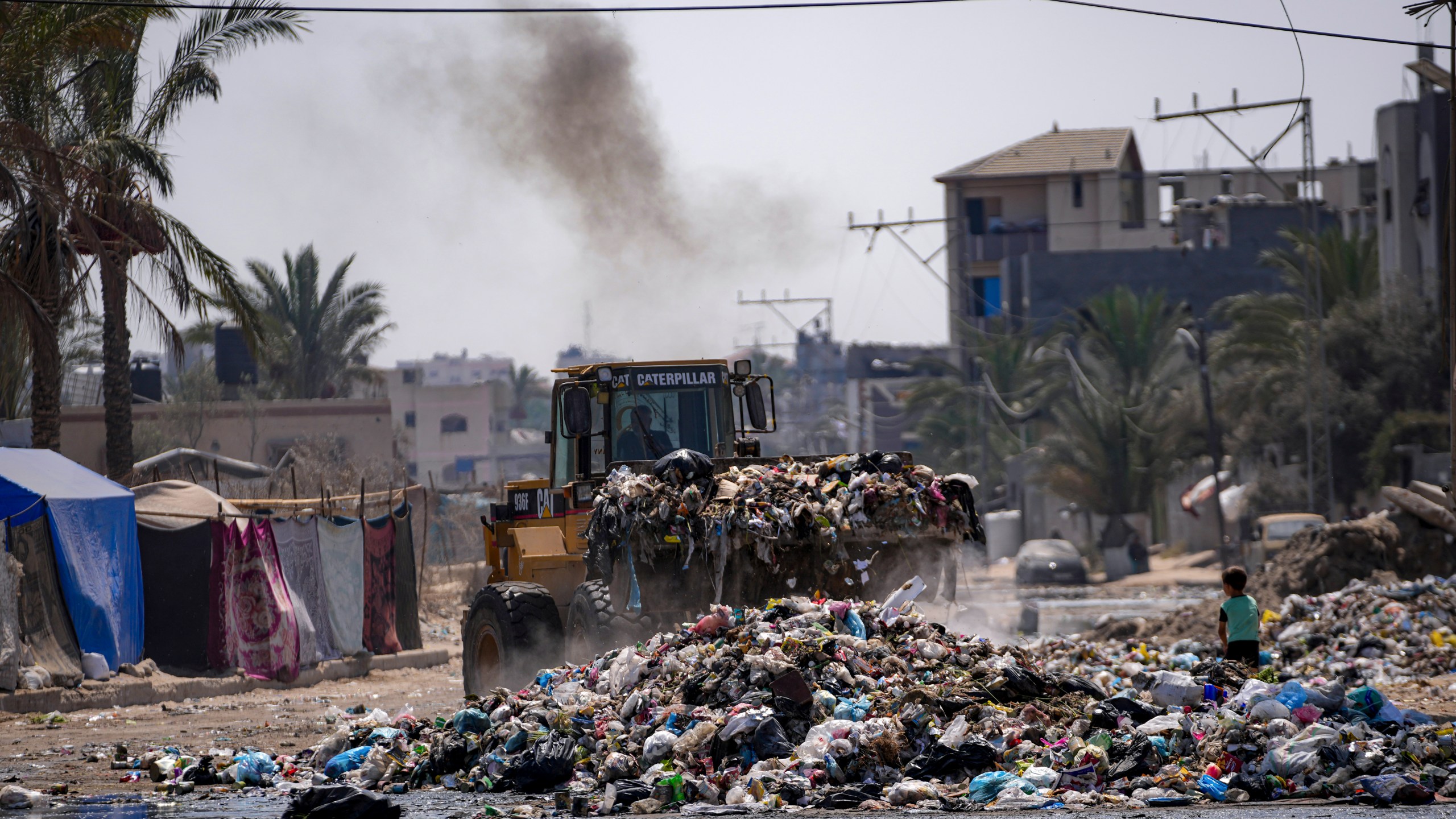 A bulldozer cleans up plastic and other waste materials at a street in Deir al-Balah, central Gaza Strip, Tuesday, Aug. 27, 2024. (AP Photo/Abdel Kareem Hana)