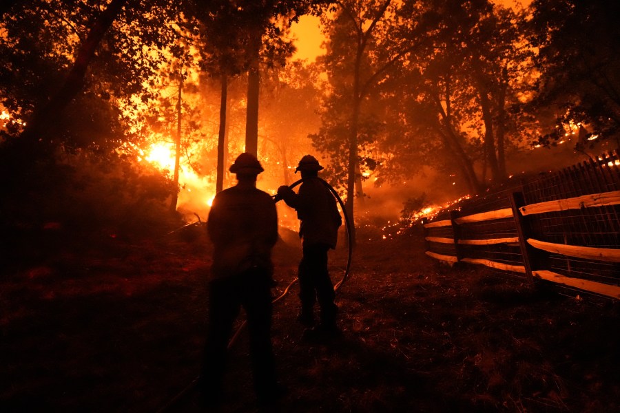 Two firefighters watch as the Bridge Fire burns near homes in Wrightwood, Calif., Tuesday, Sept. 10, 2024. (AP Photo/Jae C. Hong)