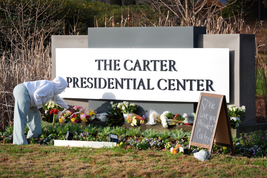 Christine Mason, of Atlanta, places flowers at entrance the The Jimmy Carter Presidential Center in Atlanta Monday, Dec. 30, 2024, in Atlanta. Formr President Jimmy Carter died Sunday at his home in Plains, Ga, at the age of 100. (AP Photo/John Bazemore )