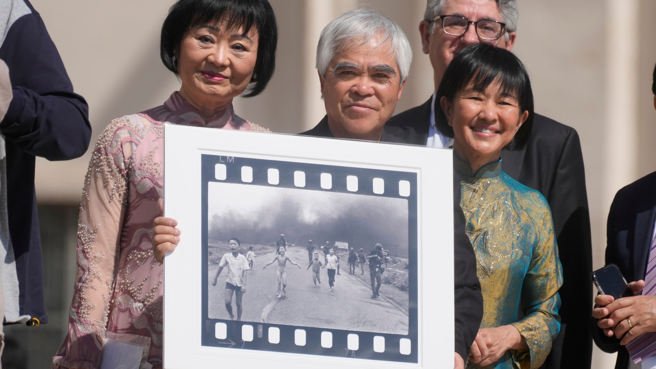 FILE - Pulitzer Prize-winning photographer Nick Ut, center, flanked by Kim Phuc, left, holds the "Napalm Girl", his Pulitzer Prize winning photo, as they wait to meet with Pope Francis during the weekly general audience in St. Peter's Square at The Vatican, Wednesday, May 11, 2022. (AP Photo/Gregorio Borgia, FILE)