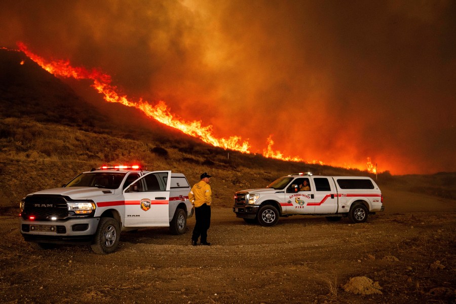 Firefighters monitor flames caused by the Hughes Fire along a roadside in Castaic, Calif., Wednesday, Jan. 22, 2025. (AP Photo/Ethan Swope)