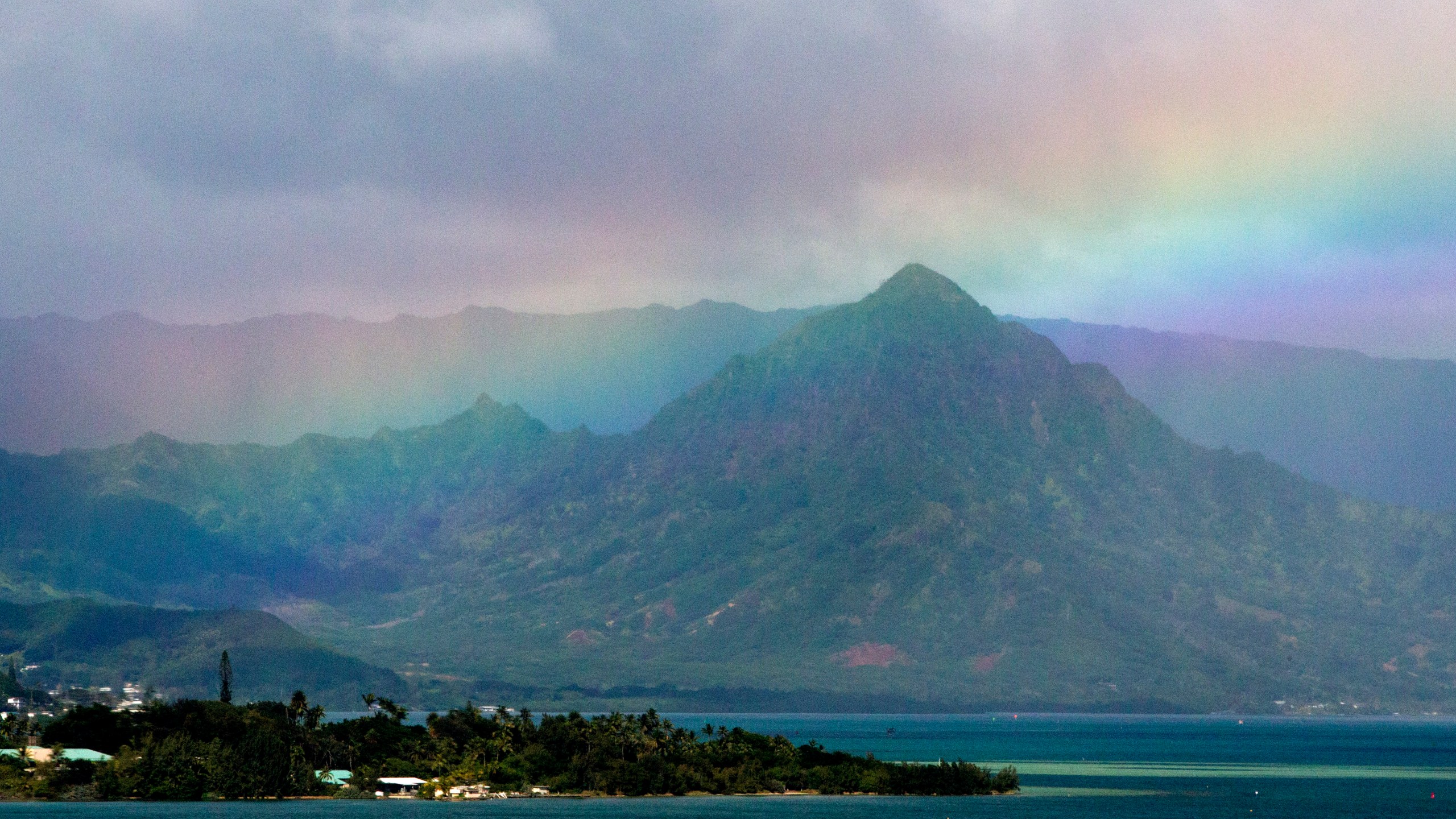 FILE -A rainbow is seen in the sky from President Barack Obama's motorcade as it passes Kaneohe Bay heading for the beach at Bellows Air Force Station, Saturday, Jan. 3, 2015, on the island of Oahu in Hawaii, on the final day of the Obama family vacation. (AP Photo/Jacquelyn Martin, File)