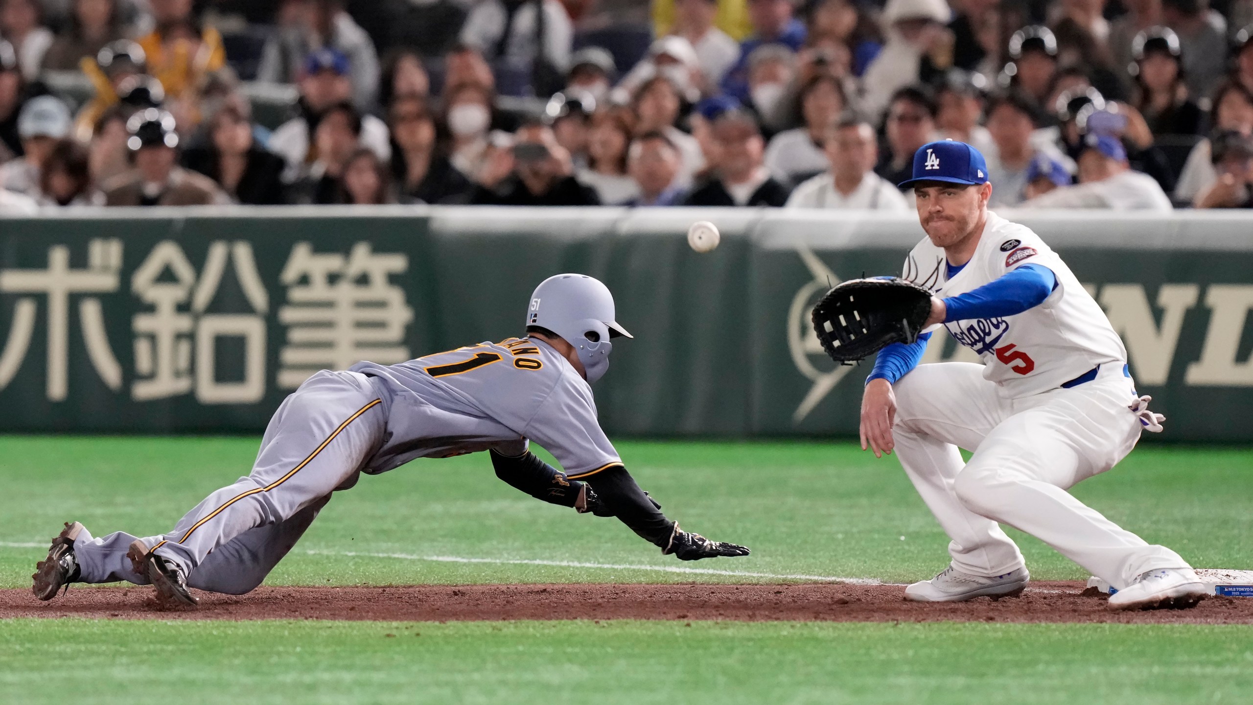 Hanshin Tigers' Takumu Nakano, left, slides into first base next to Los Angeles Dodgers' Freddie Freeman during the fifth inning in an MLB Japan Series exhibition baseball game, Sunday, March 16, 2025, in Tokyo. (AP Photo/Eugene Hoshiko)