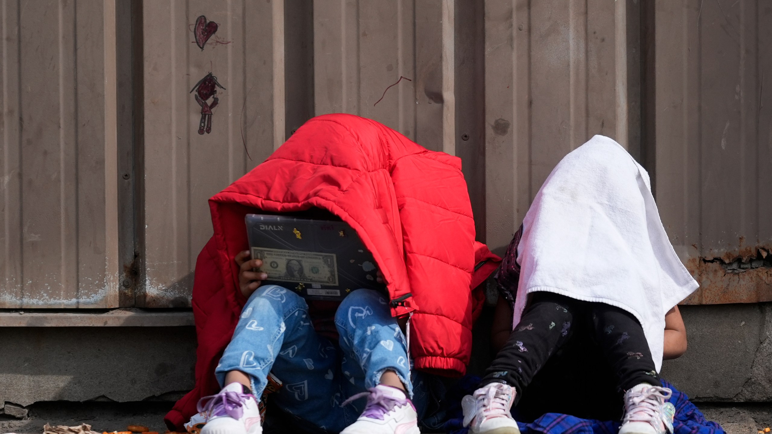 FILE - Children cover their heads as they sit outside of a migrant shelter Wednesday, March 13, 2024, in the Pilsen neighborhood of Chicago. (AP Photo/Erin Hooley, File)