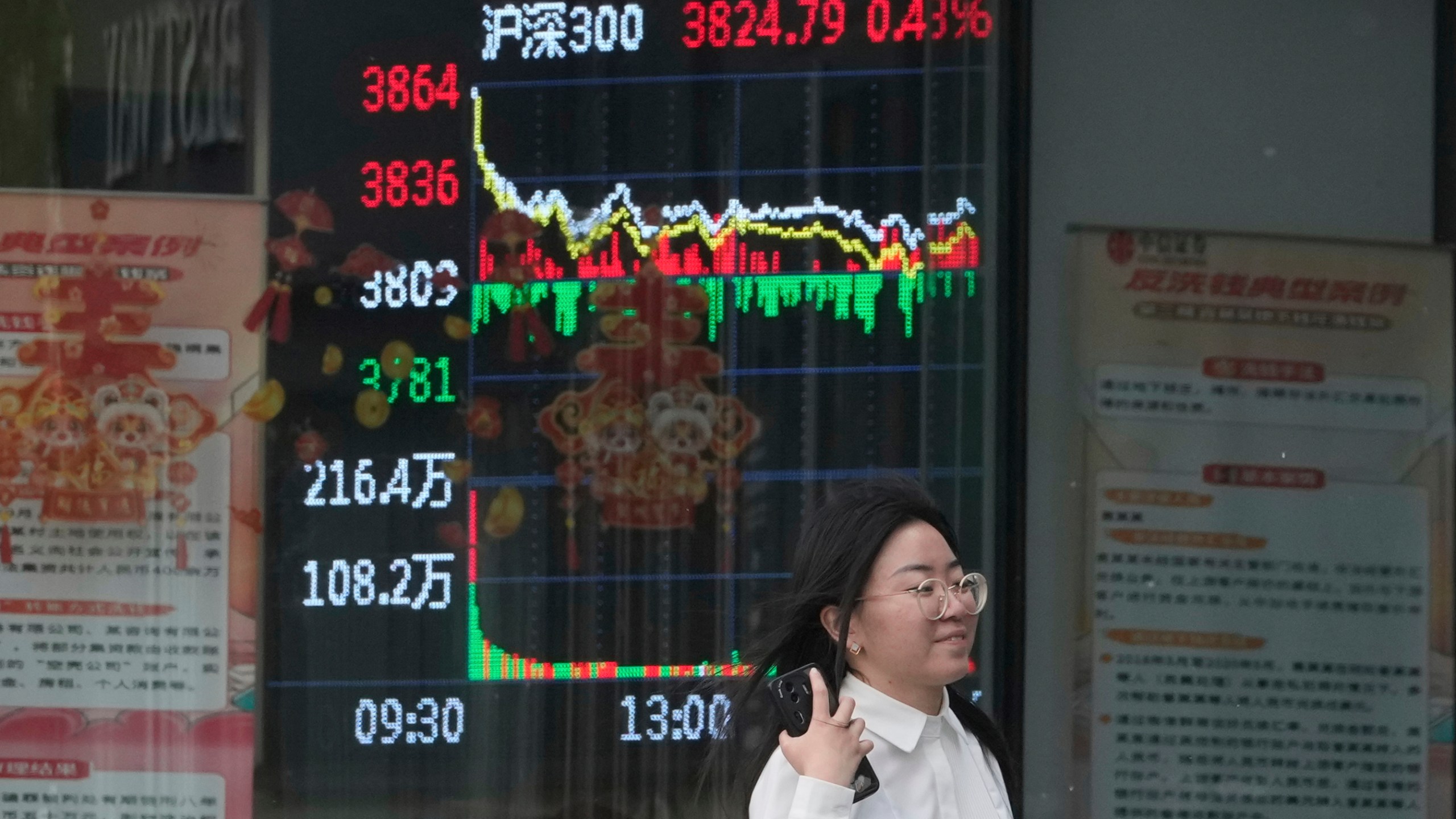A woman passes by a stock index at a brokerage in Beijing, Wednesday, May 7, 2025. (AP Photo/Ng Han Guan)