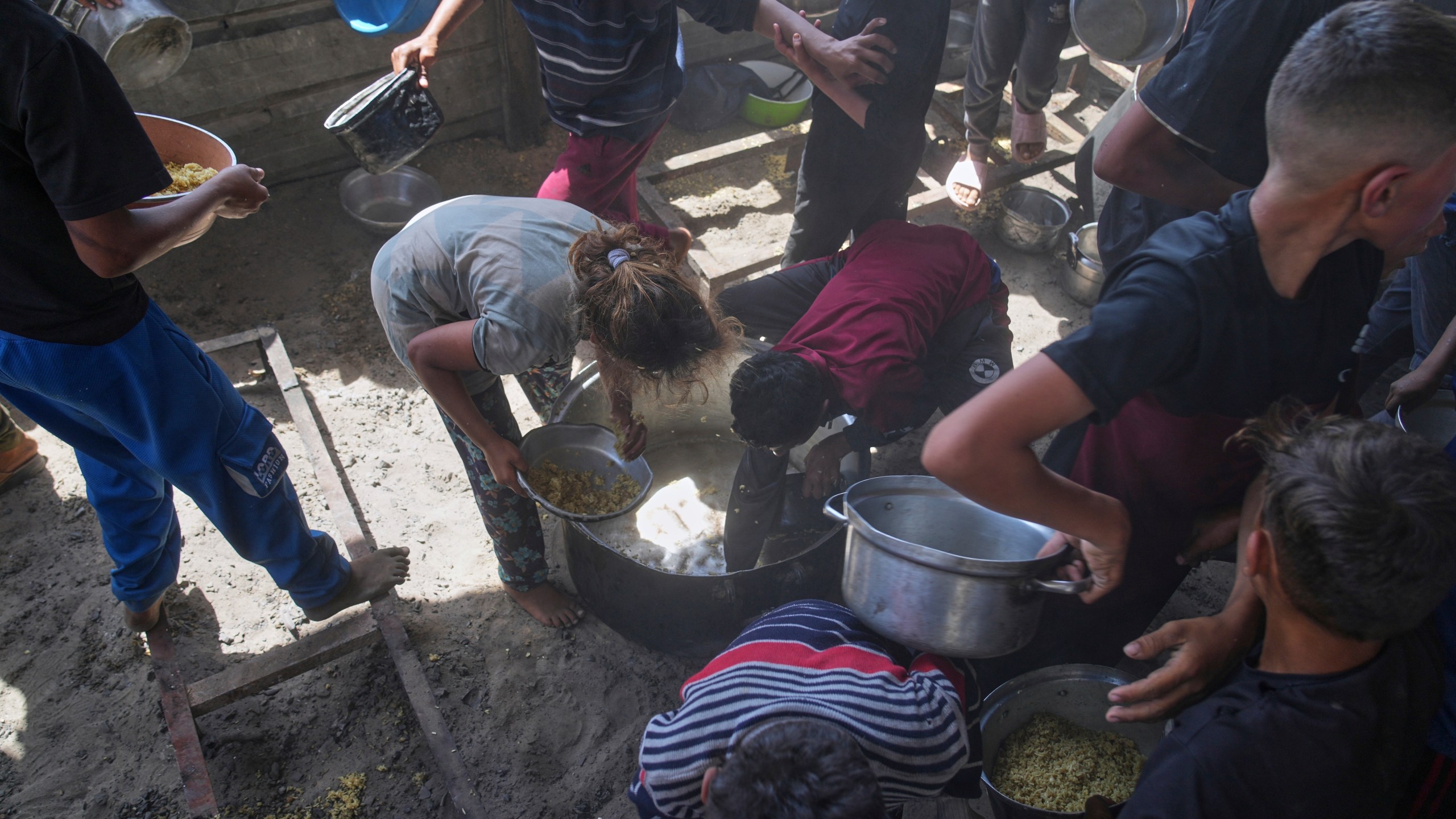 Palestinian children scrape a pot for leftover food after all meals were distributed at a community kitchen in Khan Younis, southern Gaza Strip, on Friday, May 9, 2025. (AP Photo/Abdel Kareem Hana)