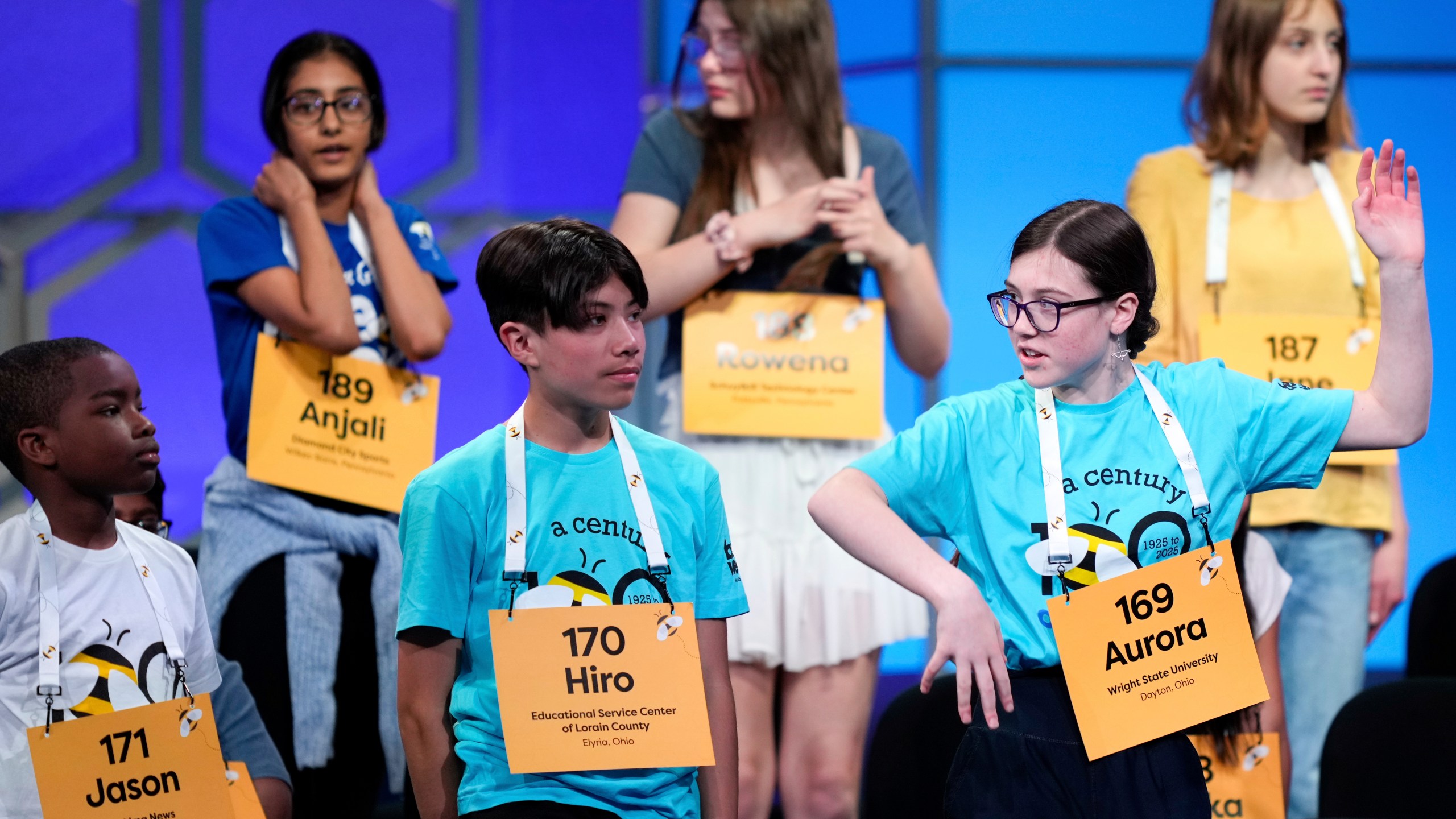 Aurora Ottilie Spisak, 14, of Dayton, Ohio, front right, stretches during a commercial break in the first preliminary round of the Scripps National Spelling Bee, Tuesday, May 27, 2025, in Oxon Hill, Md. (AP Photo/Julia Demaree Nikhinson)