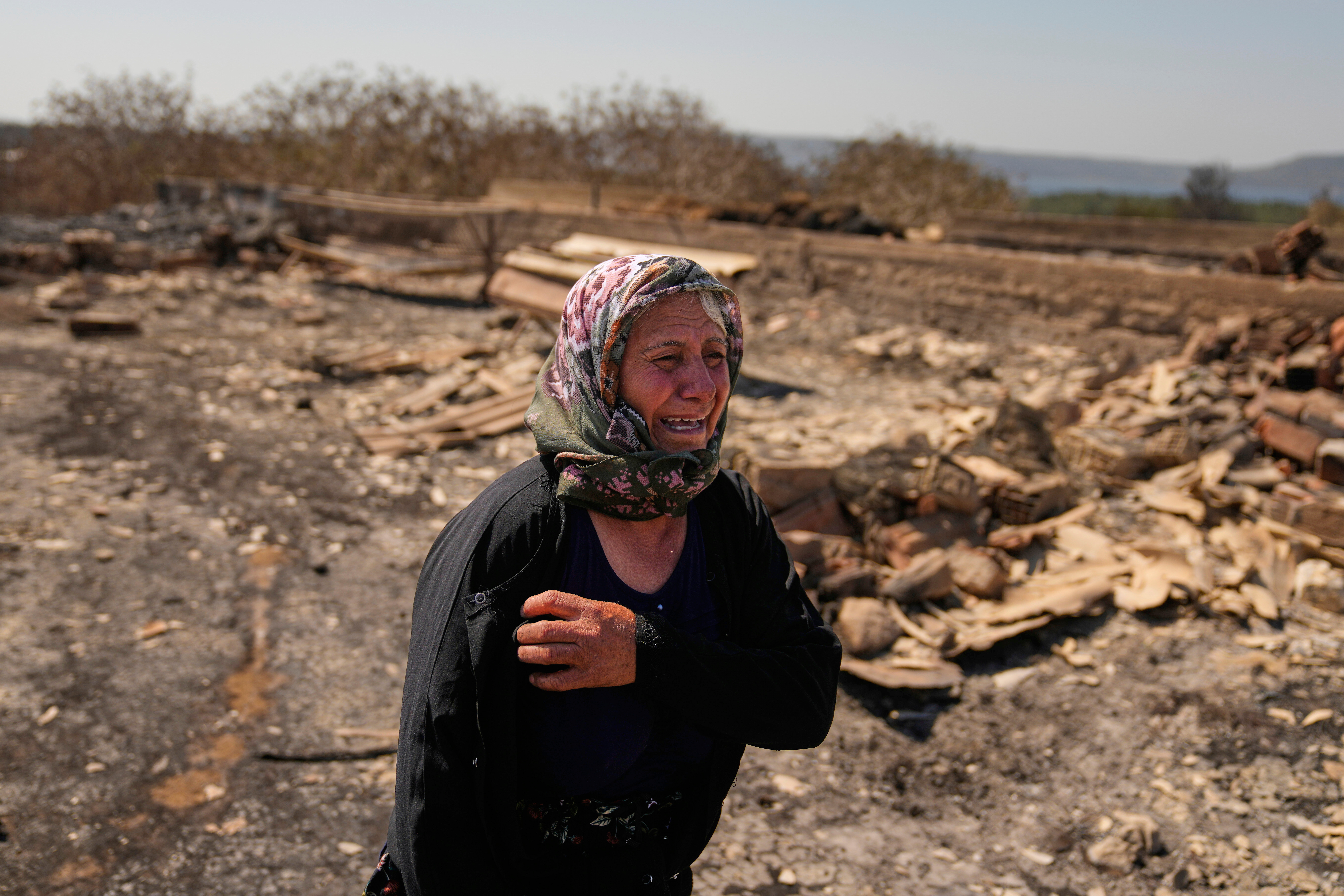 Local farmer Turkan Ozkan cries next to her destroyed home after a fire in Guzelyeli, in the outskirts of Canakkale, northwest Turkey, Tuesday, Aug. 12, 2025. (AP Photo/Khalil Hamra)