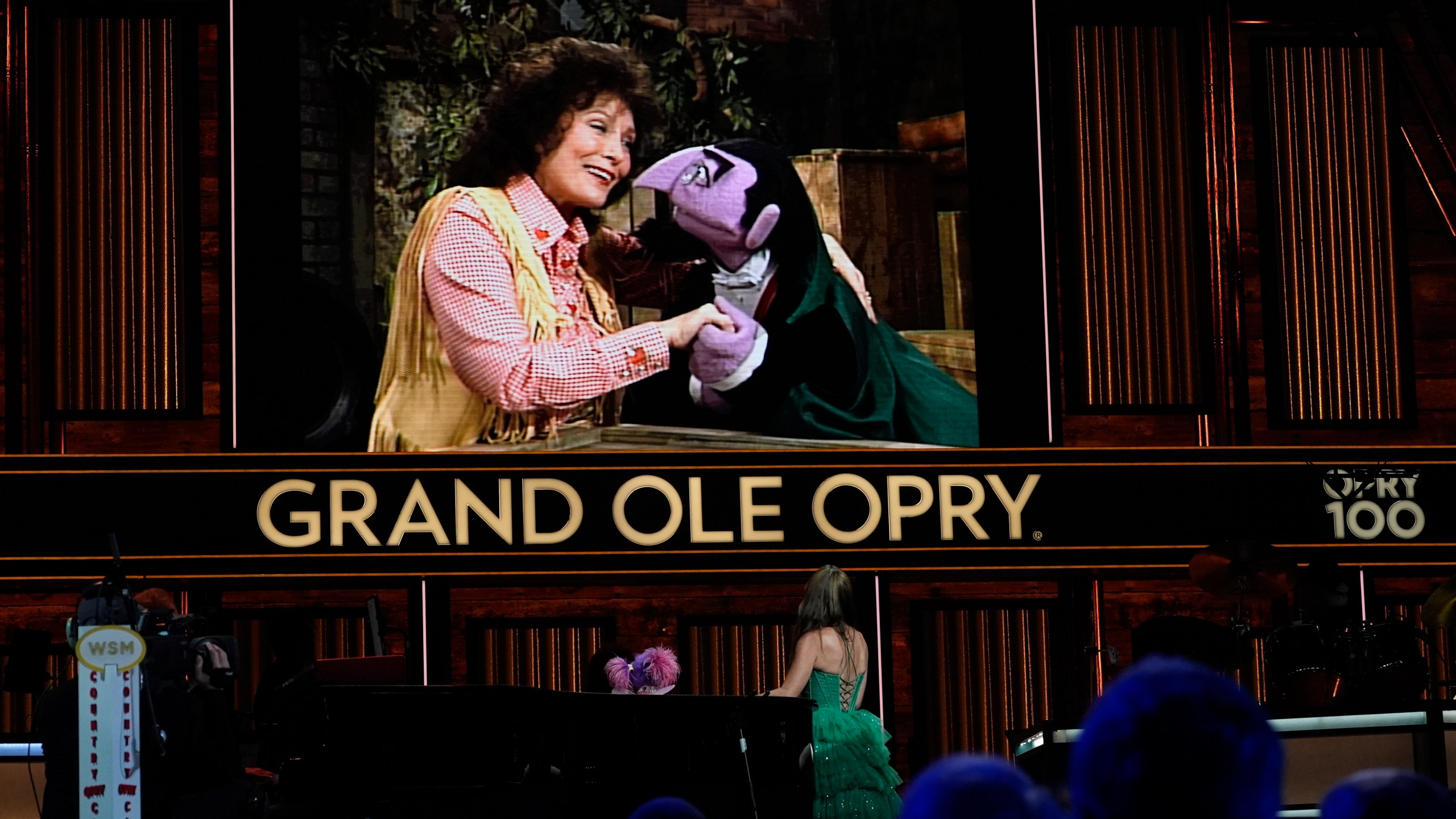 A video of Loretta Lynn and Count von Count of Sesame Street is displayed as puppet Abby Cadabby and Tayla Lynn, below, perform at the Grand Ole Opry, Thursday, Aug. 14, 2025, in Nashville, Tenn. (AP Photo/George Walker IV)