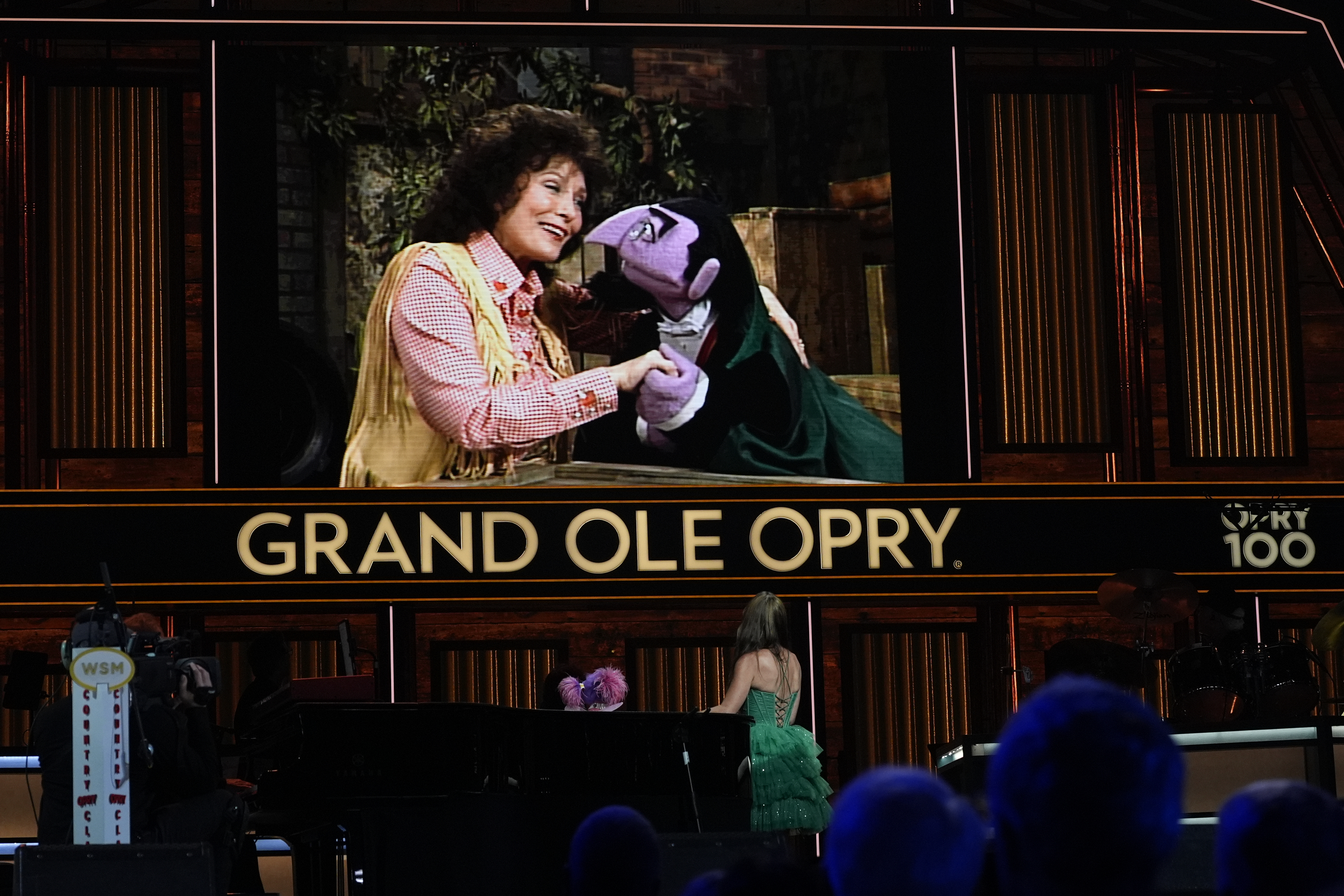 A video of Loretta Lynn and Count von Count of Sesame Street is displayed as puppet Abby Cadabby and Tayla Lynn, below, perform at the Grand Ole Opry, Thursday, Aug. 14, 2025, in Nashville, Tenn. (AP Photo/George Walker IV)