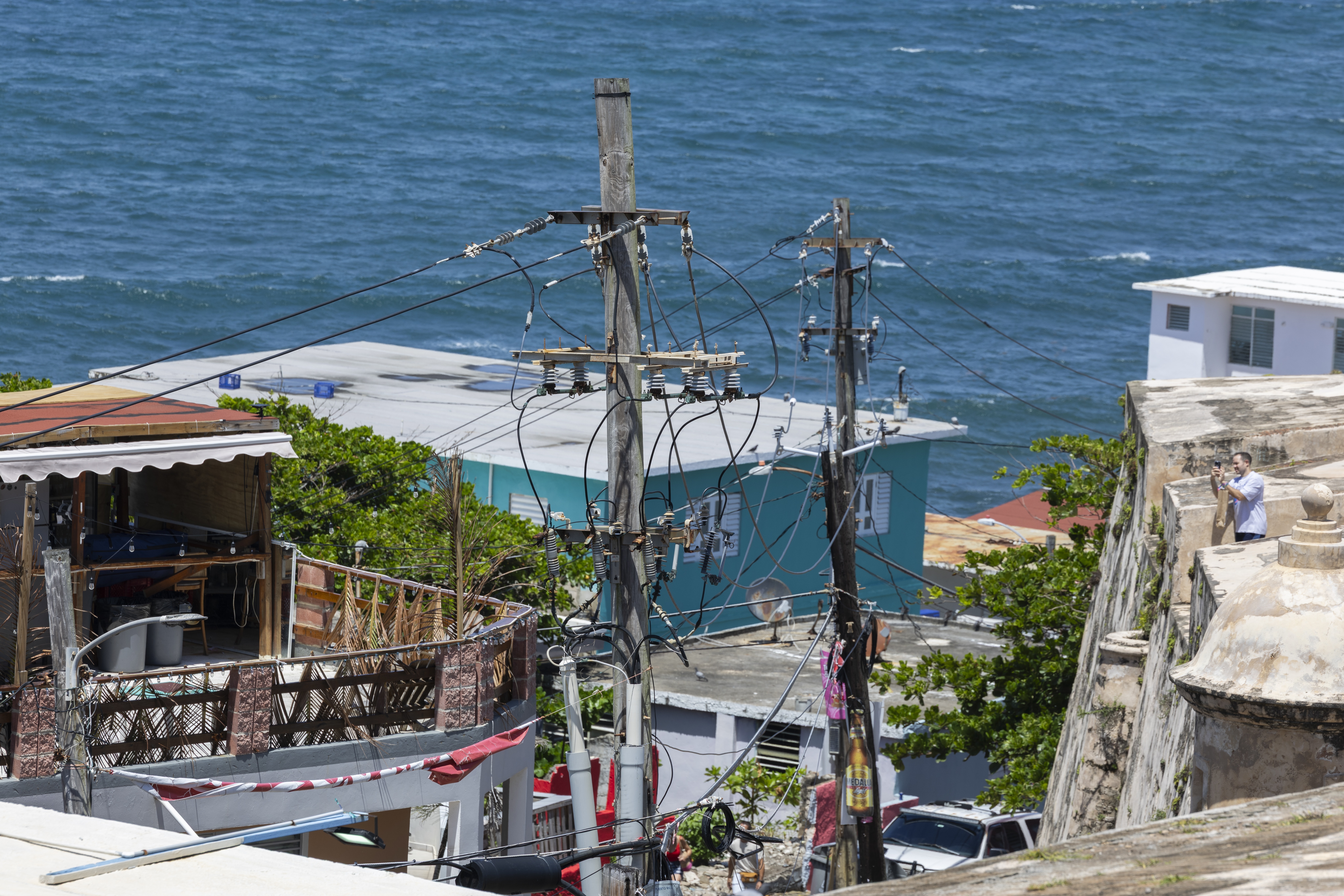 Power lines and utility poles stand in front of La Perla neighborhood along the coast in Old San Juan, Puerto Rico, as Hurricane Erin approaches, Friday, Aug. 15, 2025. (AP Photo/Alejandro Granadillo)