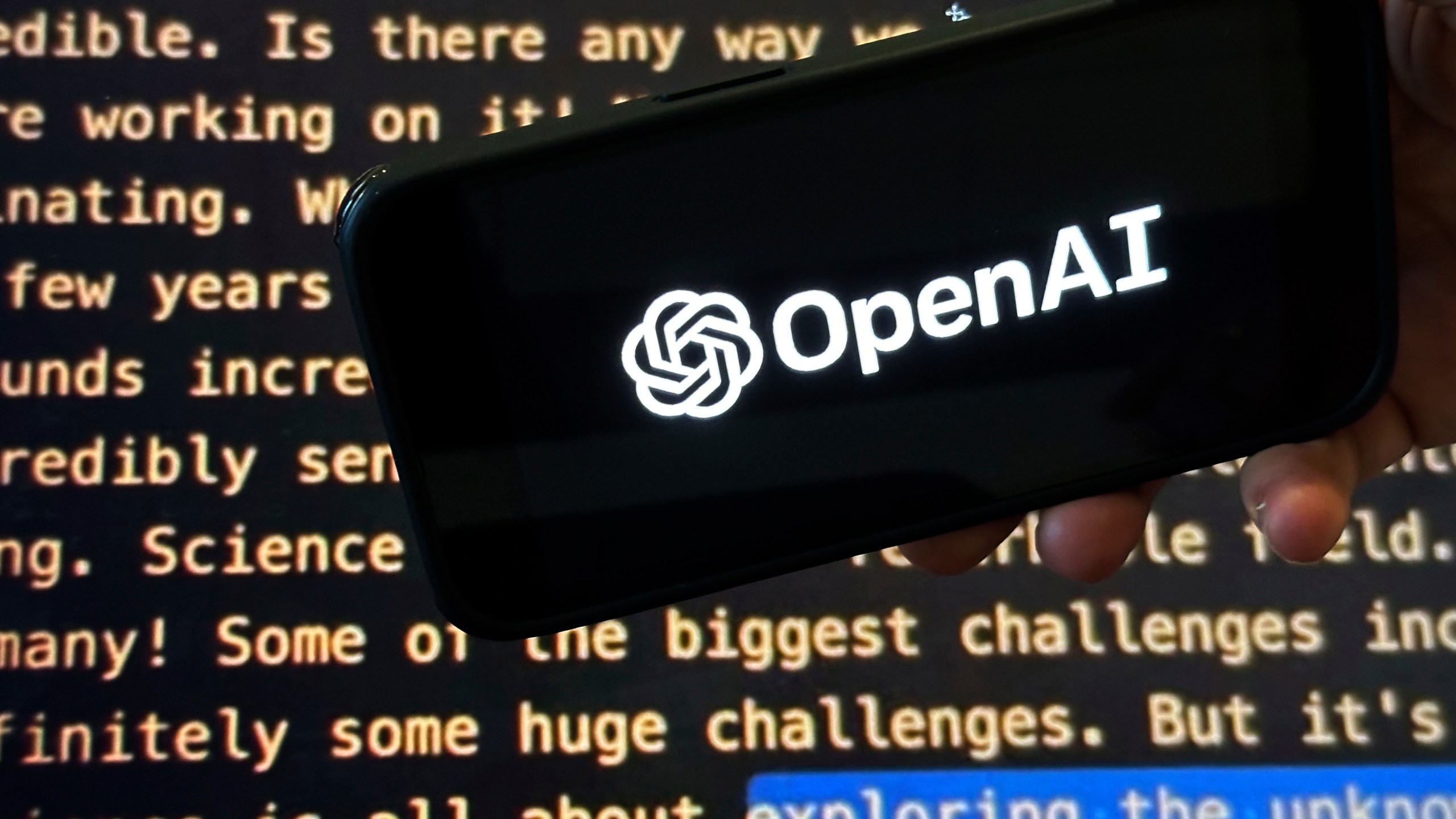 FILE - The OpenAI logo appears on a mobile phone in front of a screen showing part of the company website in this photo taken on Nov. 21, 2023 in New York. (AP Photo/Peter Morgan, File)
