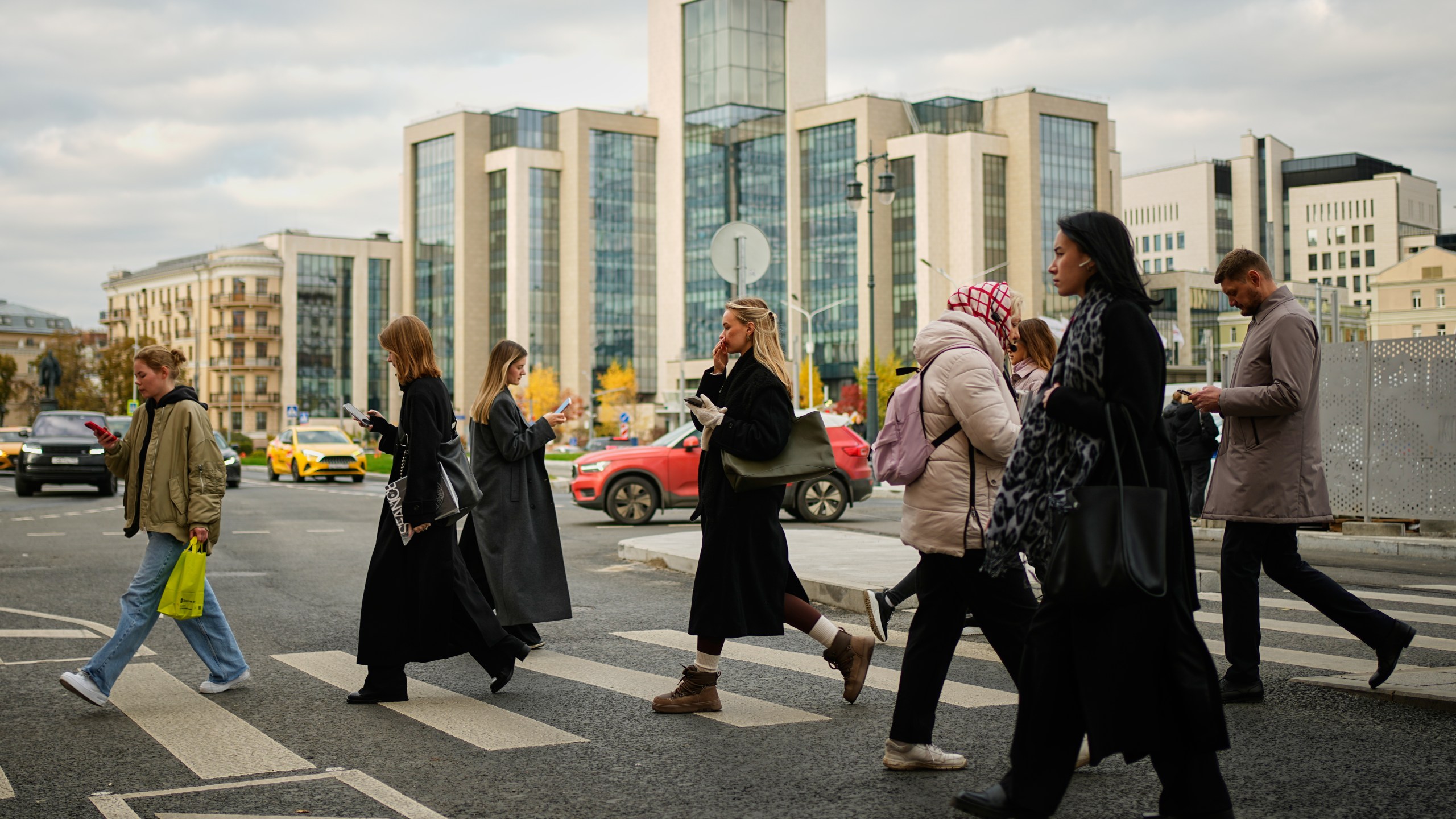 People cross a street, with Russian oil company Lukoil's headquarters seen in the background, in Moscow, Russia, Thursday, Oct. 23, 2025. (AP Photo/Pavel Bednyakov)